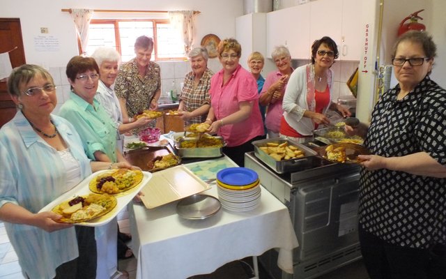 Die groep dames van die NG Vrouediens se Uitreikaksie â€œin aksieâ€ in die kombuis met die geurige ete 